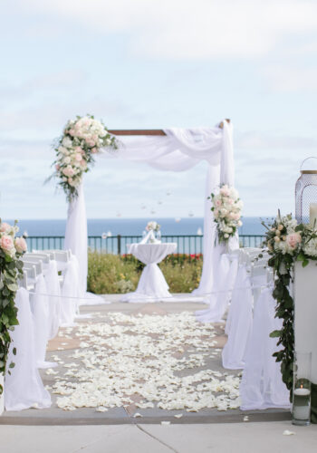 Wood arch with white sheers with florals in white and blush at the Heritage Park in Dana Point, CA.